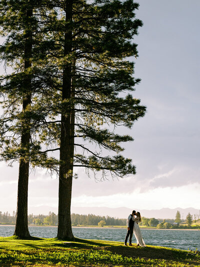 Bride and groom share a kiss under tall pine trees during their Glacier National Park wedding.
