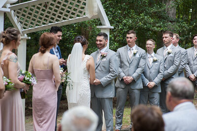 bride in fitted beaded detailed wedding dress holding hands with Groom in grey tux during ceremony at eden try winery