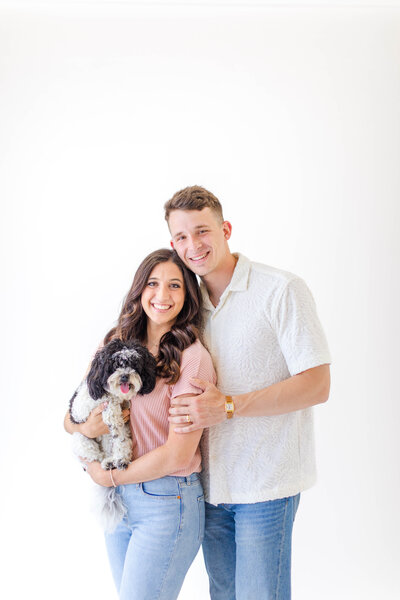 Nashville wedding photographer Brooke Elliott wearing a pink shirt and light wash jeans, her husband Isaac wearing a white shirt and medium wash jeans, and their black and white cockapoo named Bristol