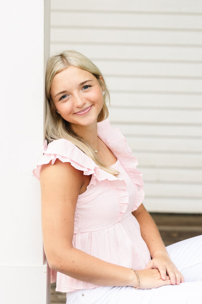 a senior girl wearing a pink shirt leaning against a pole for her senior session