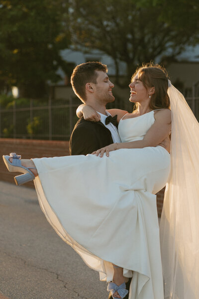 Man wearing Tuxedo carrying a women wearing wedding dress and long vail