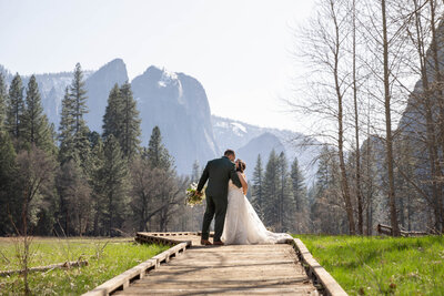 A bride and groom kiss on a wooden boardwalk in Yosemite after their adventure elopement day.