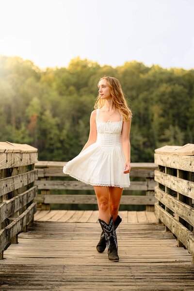 sun valley senior walks in cowboy boots looking off to her right wearing a white dress with the sun on her hair