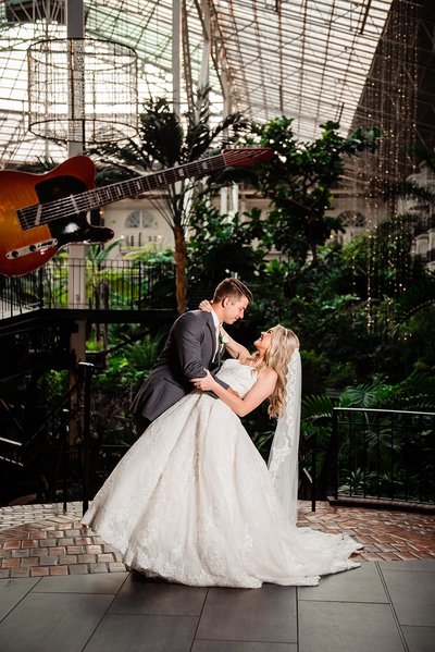 Groom dipping bride wearing a Cinderella ballgown on the 2nd floor in the Gaylord Opryland atrium with the large guitar hanging in the background