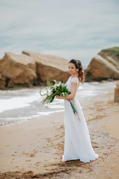 bridal portrait on sandy beach with rocks in the background