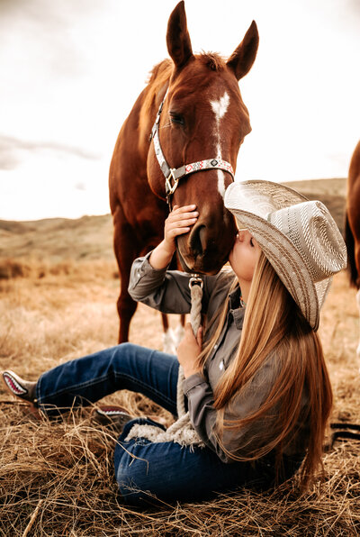 Girl sits on the ground and kisses her horse's nose