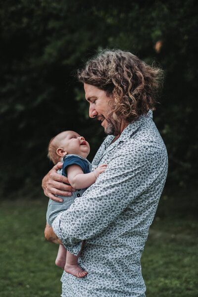 Father with chin length curly hair holding his baby son and smiling at each other