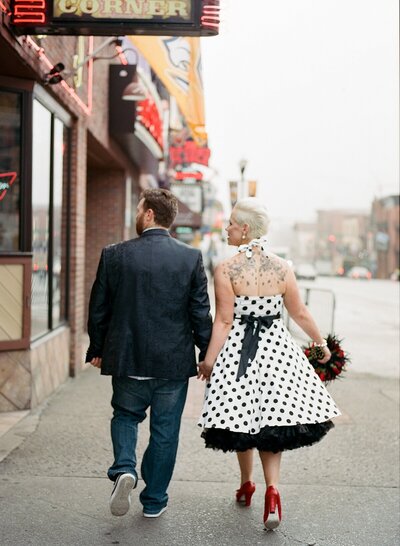 The 1950s pinup bride and her rockabilly groom in jeans and a silk suit jacket walking down Broadway in downtown Nashville