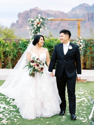 Bride in classic wedding dress holds and hands with and smiles at her groom