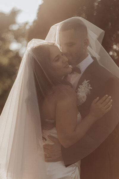 Sunlit bride and groom embrace, backlit for a warm, ethereal glow.