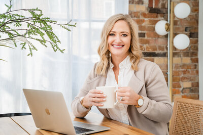 Newborn coach working at her desk drinking a cup of coffee and smiling at camera