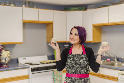 A woman holding cupcakes with a kitchen backdrop
