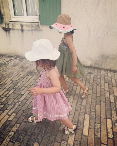 Two little girls walking up a cobbled street in Ile De Re in summer dresses and sun hats.