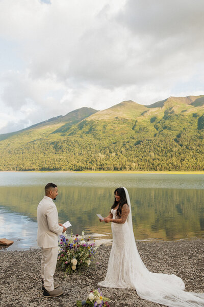 bride and groom walking on a snowy mountain with the sun shining in the back
