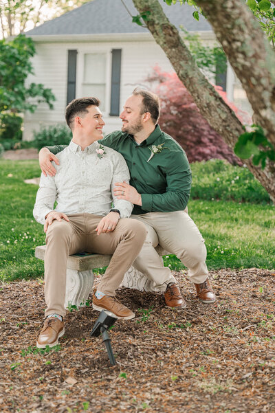 A glowing same sex couple snuggling up under a tree at Highrock Farms by JoLynn Photography, a Raleigh wedding photographer