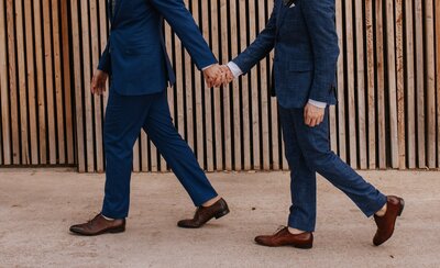 male couple in blue suits hold hands as they walk