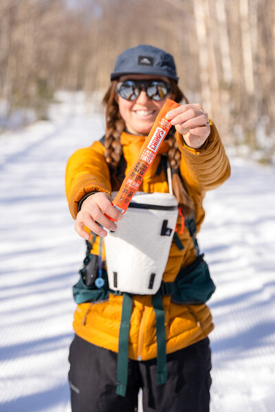 Meredith holding Chomps meat sticks snack while cross country skiing