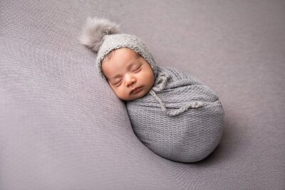 newborn photoshoot with baby wrapped in gray