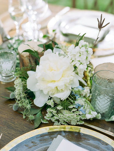 Close up of reception table decorated with large white flower, gold rimmed plates, and glass candles