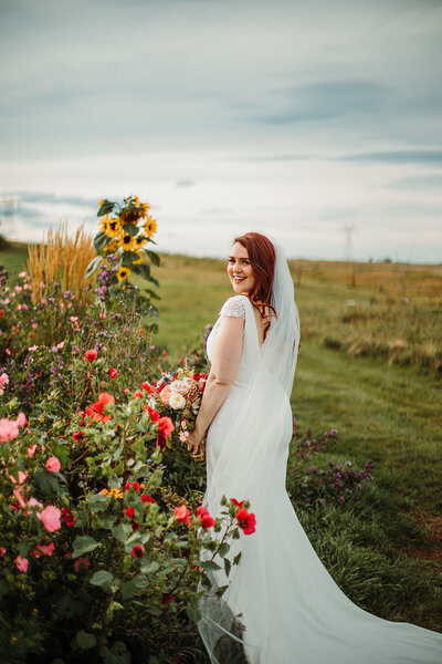 bride standing beside bright flower bed, field behind her
