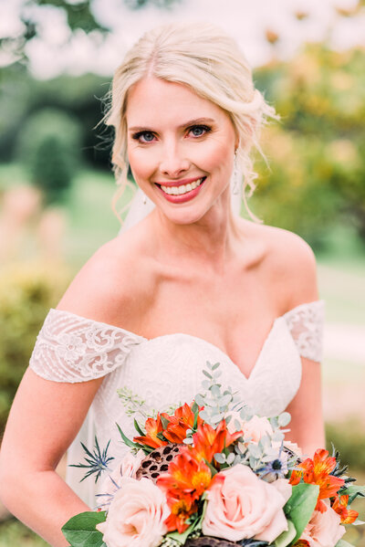 Bride smiling holding wedding bouquet of orange and peach tone flowers by Grand Rapids wedding photographer Stephanie Anne