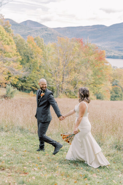 Light and airy photograph of a couple holding hands and walking during their elopement in the Adirondacks near Lake George. It was peak fall foliage on their elopement day in Upstate NY.