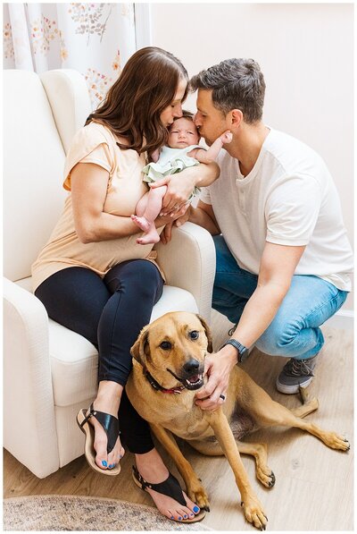mom and dad are kissing and loving on their new baby girl while their family dog is hanging out with them.  This was taken during an in home lifestyle newborn session in Wexford PA