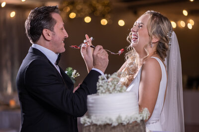 Blonde bride laughing as she trades the first bite tradition with her groom at The District Event Venue in Clearwater, Florida - A joyful and lighthearted moment of love and celebration