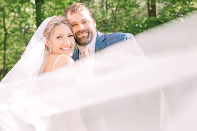 A smiling couple surrounded by a veil sweeping across the frame at sunset by JoLynn Photography