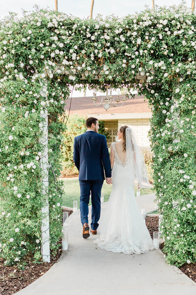 bride and groom walking through a floral arch on their wedding day