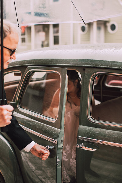 Msn opens the door of a vintage car for a bride
