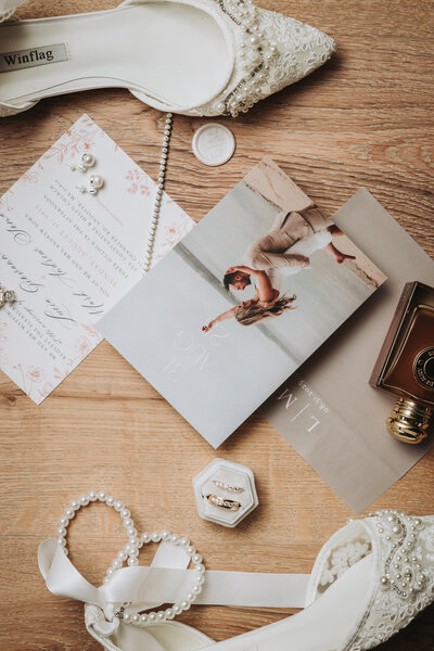 Wedding flatlay photo of rings, pearls, invitations, and photo