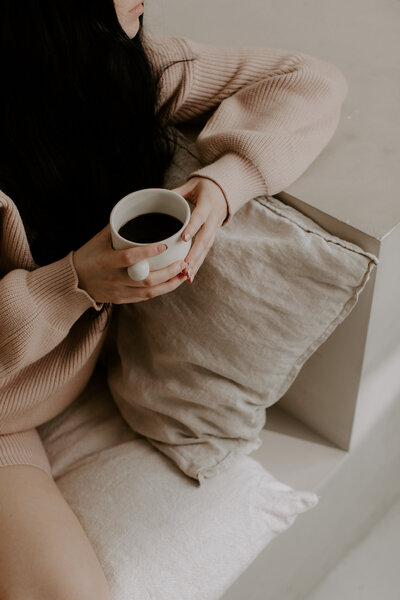 Woman in tan sweats sitting on a couch with a mug of coffee