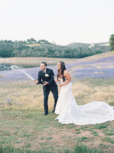 A couple that eloped in El Dorado Hills at Folsome Lake during the Lupine season as they pop a champagne bottle to celebrate their wedding vows.