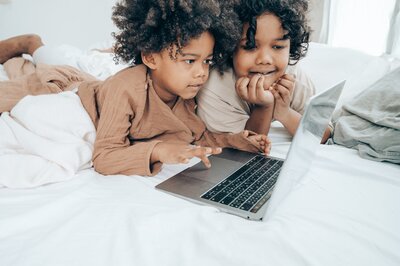 Black siblings using laptop for homeschool activity on bed