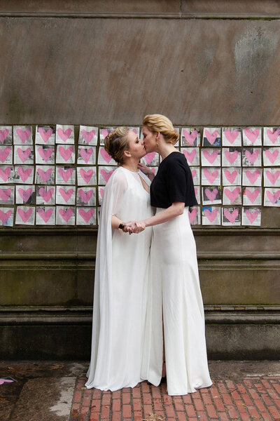 Two bride kiss in front of illegal street art at the Bethesda Terrace in Central Park
