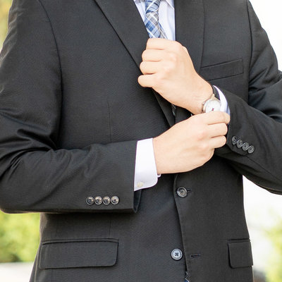 Wedding details Groom adjusting sleeve showing his round watch wearing a black jacket and blue tie