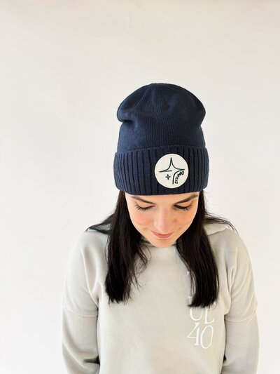 woman looking down wearing navy cuffed beanie with true40 icon