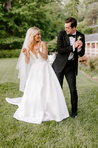 Groom in a white jacket is dipping his bride with their wedding party behind them cheering.