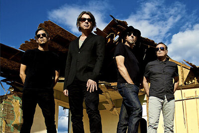 Band photo 5440 standing in front of dilapidated house blue sky and clouds above them