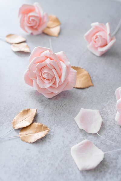 blush pink roses and gold rose leaves sit atop a replica surface