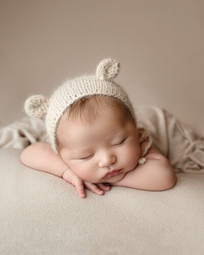 A sleeping newborn rests its head on its hands in a knit bonnet with ears posed by a New Orleans Family, Maternity & Newborn Photographer