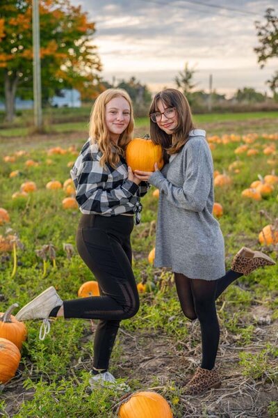 two woman standing in a field holding pumpkins at Pierson's Orchard in Ionia Michigan