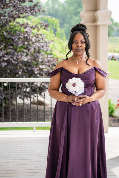 Bridesmaid in flowing purple gown holding bouquet on porch – photographed by wedding photographer Niko Coric – Lumen Clarity Media