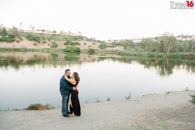 Engaged couple embrace each other next to the lake at Laguna Niguel Regional Park