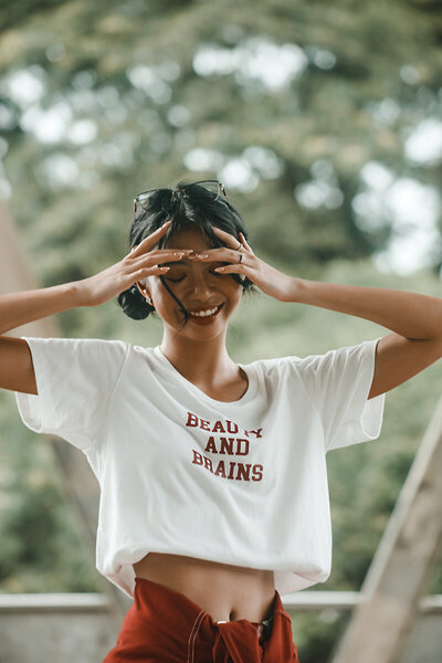A happy woman wearing a shirt that says "beauty & brains".  Showing the positive outcome of therapy for self-esteem in Manhattan with a confidence counselor. Start feeling better with CBT for self-esteem today!