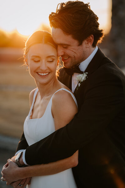 Bride and groom cuddling at sunset