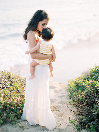 A mother kisses her baby on the head on  the bluffs at El Matador beach in Malibu during their family portrait session with photographer Daniele Rose