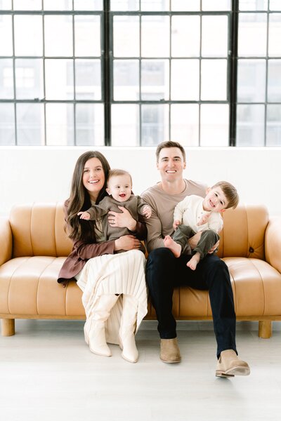 Family of mom and dad with two young sons smiling on a studio couch