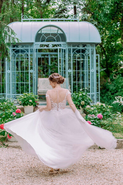 bride walking away from camera with flared dress skirt with a bird cage style gazebo and swing in the background